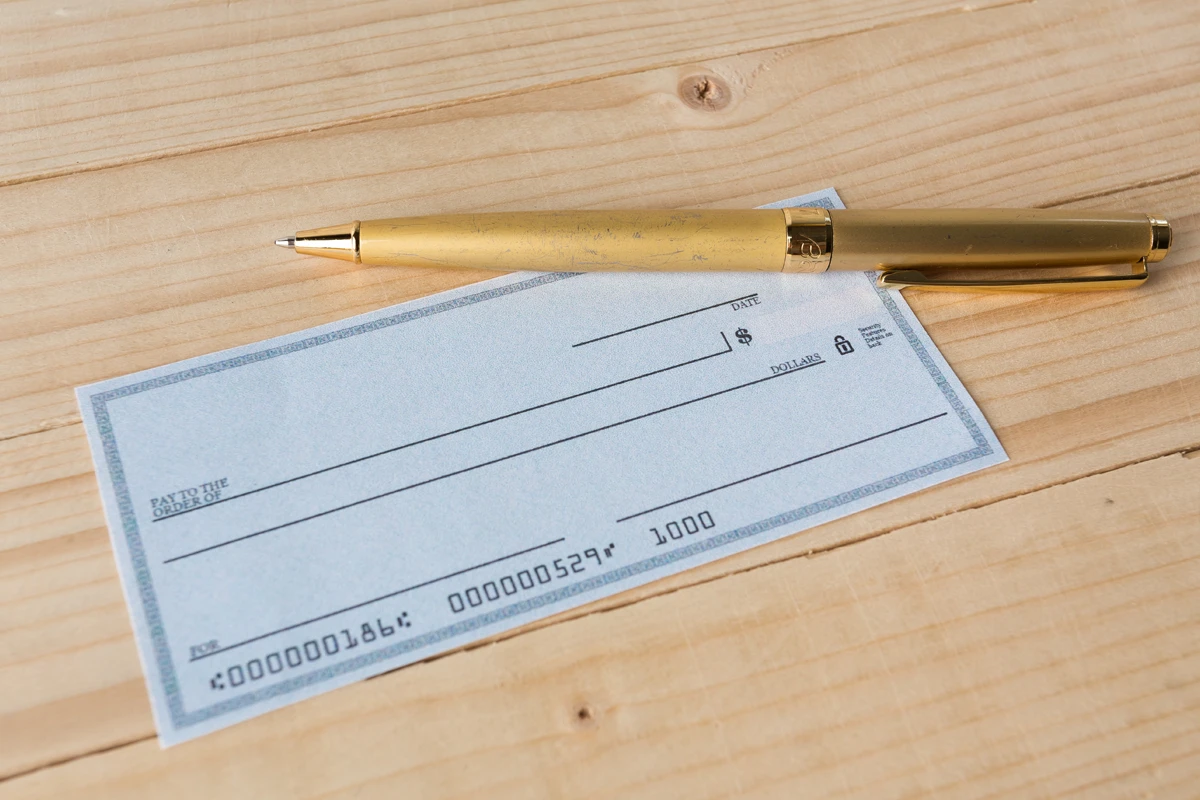 A blank check and a gold pen resting on a wooden surface.