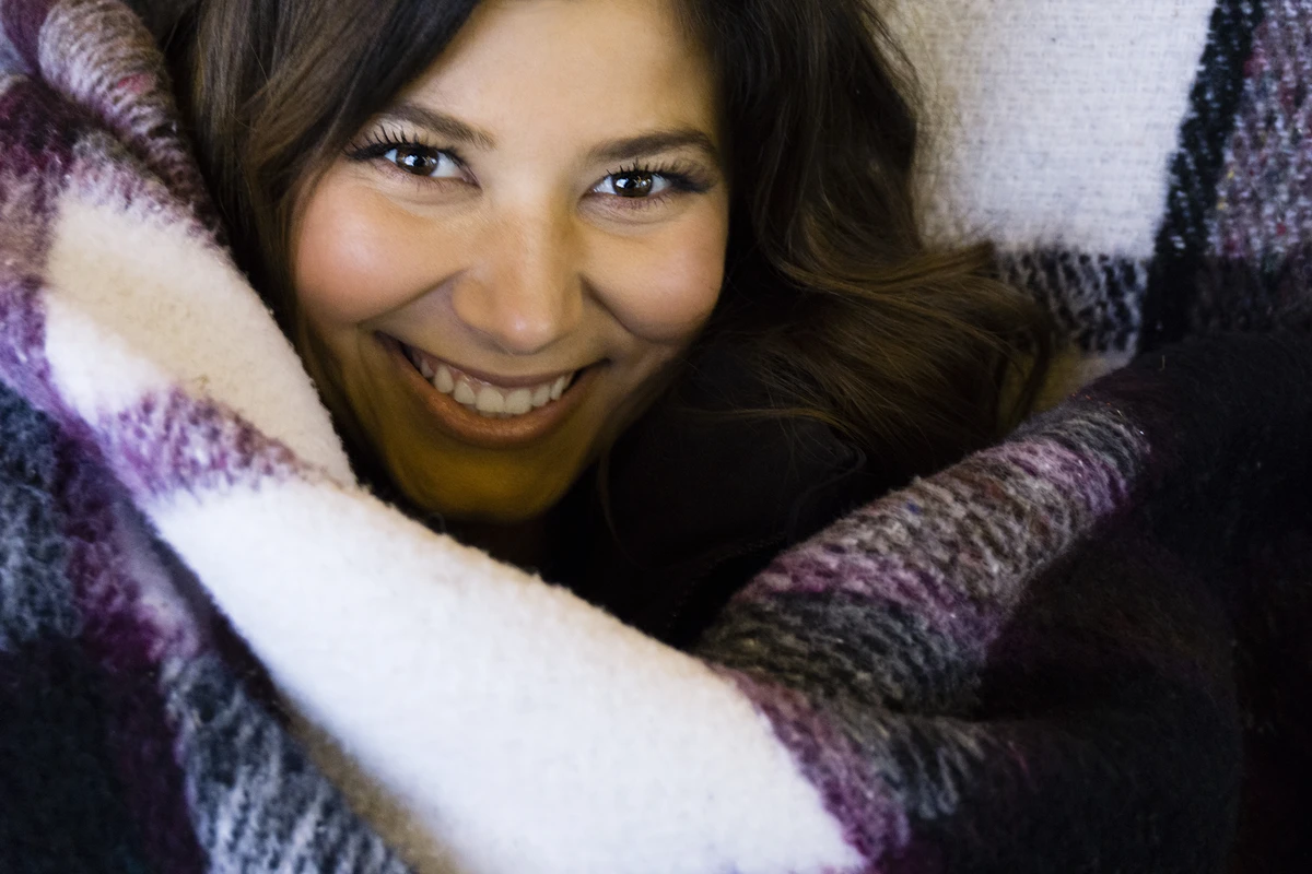 Smiling woman wrapped in a cozy, patterned blanket, exuding warmth and comfort.