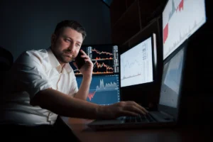 Man in a white shirt analyzes financial data on multiple screens while talking on the phone. become a day trader