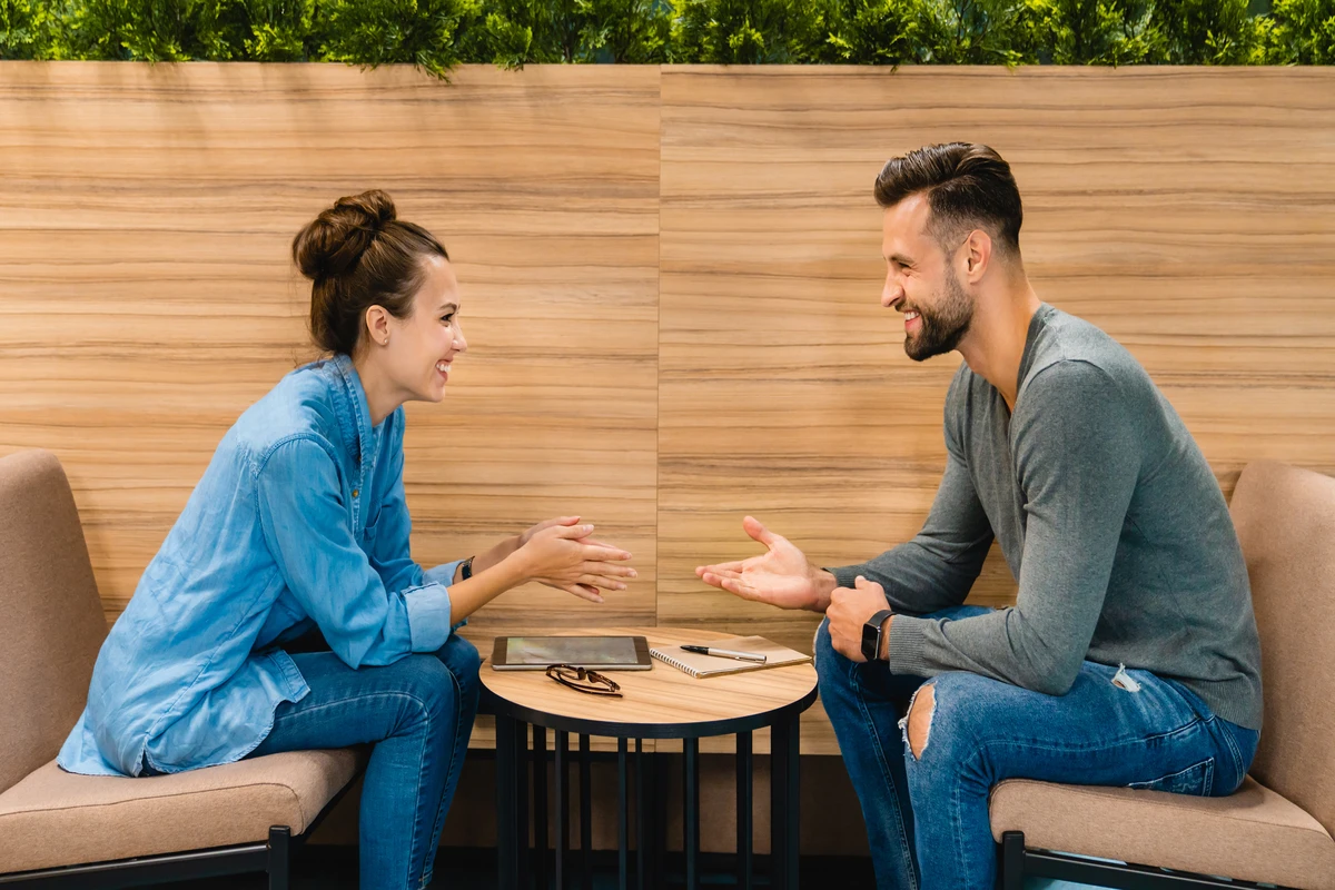 Two people engaged in a lively conversation while seated at a small table in a modern setting.
