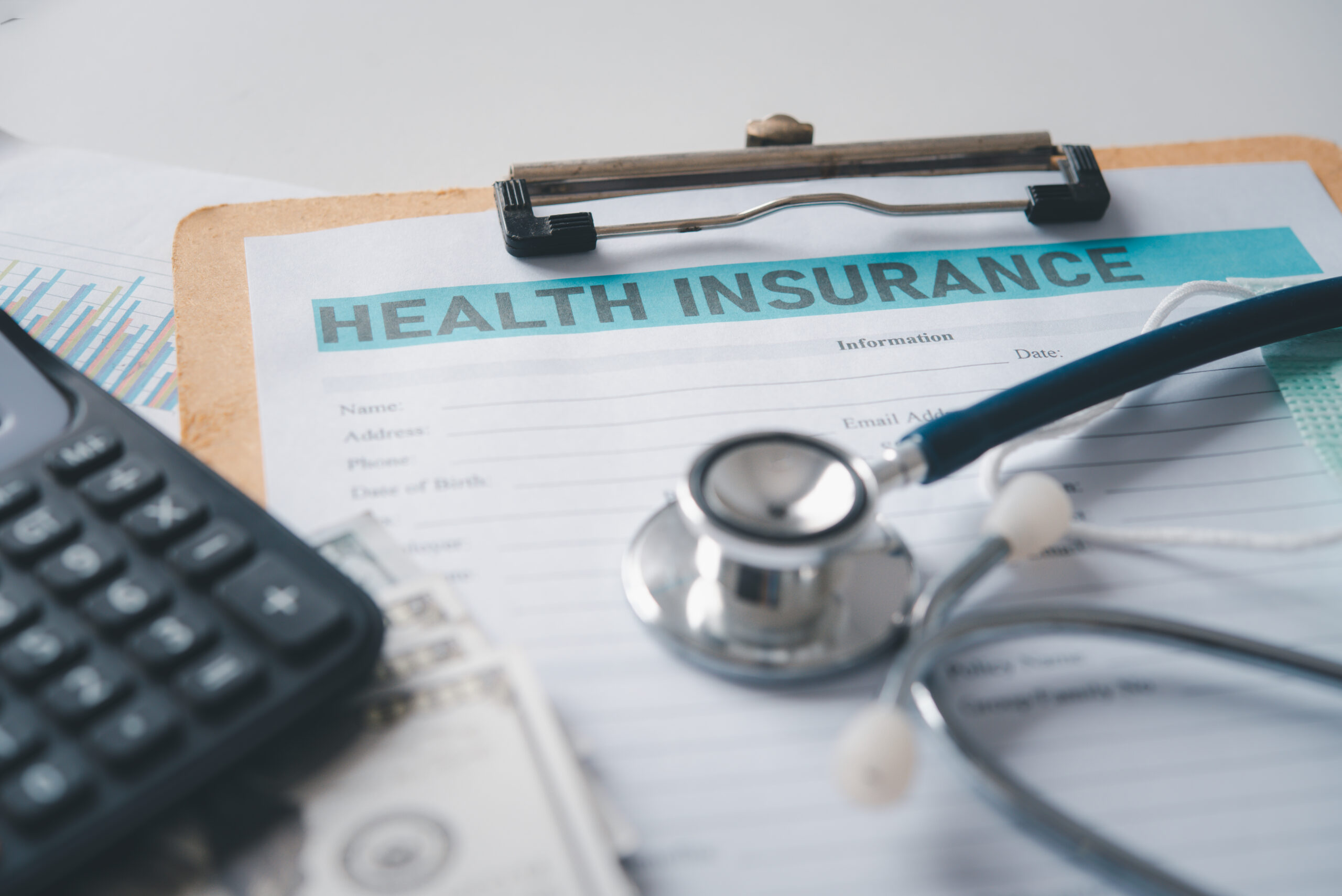 Health insurance form on a clipboard with a stethoscope and calculator, alongside cash and financial documents.