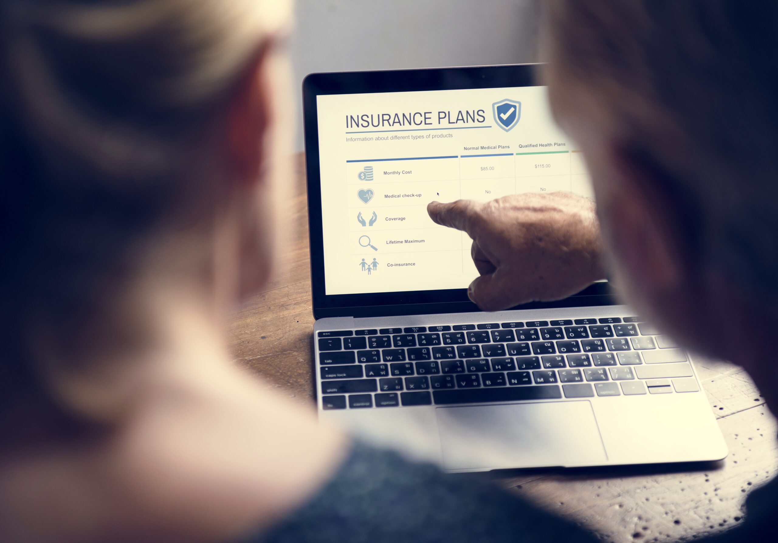 Two people reviewing insurance plans on a laptop, with one pointing at the screen's details. do young people need insurance