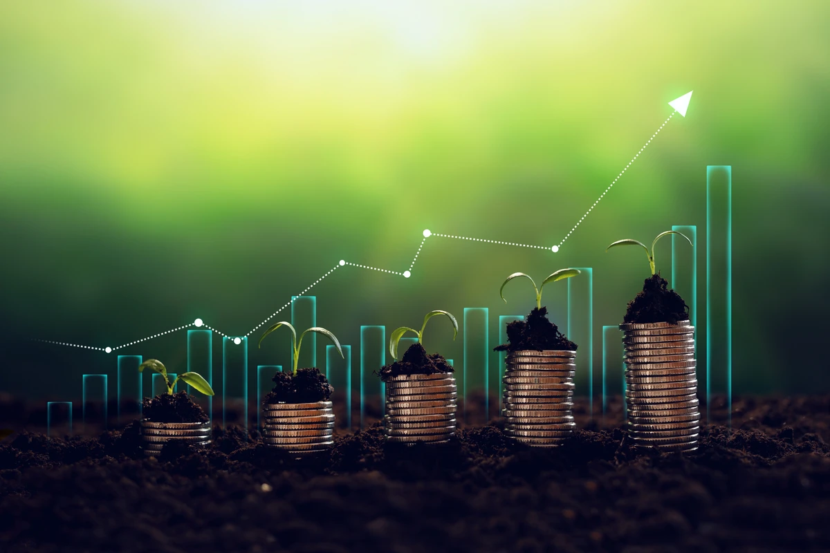 Growing plants on stacks of coins with a rising graph in the background, symbolizing financial growth and sustainability.