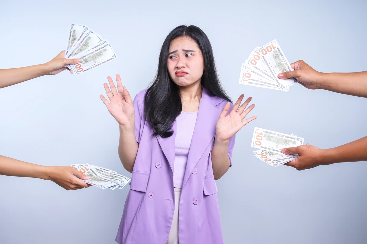 A woman in a purple blazer looks uncomfortable as multiple hands offer her stacks of cash.