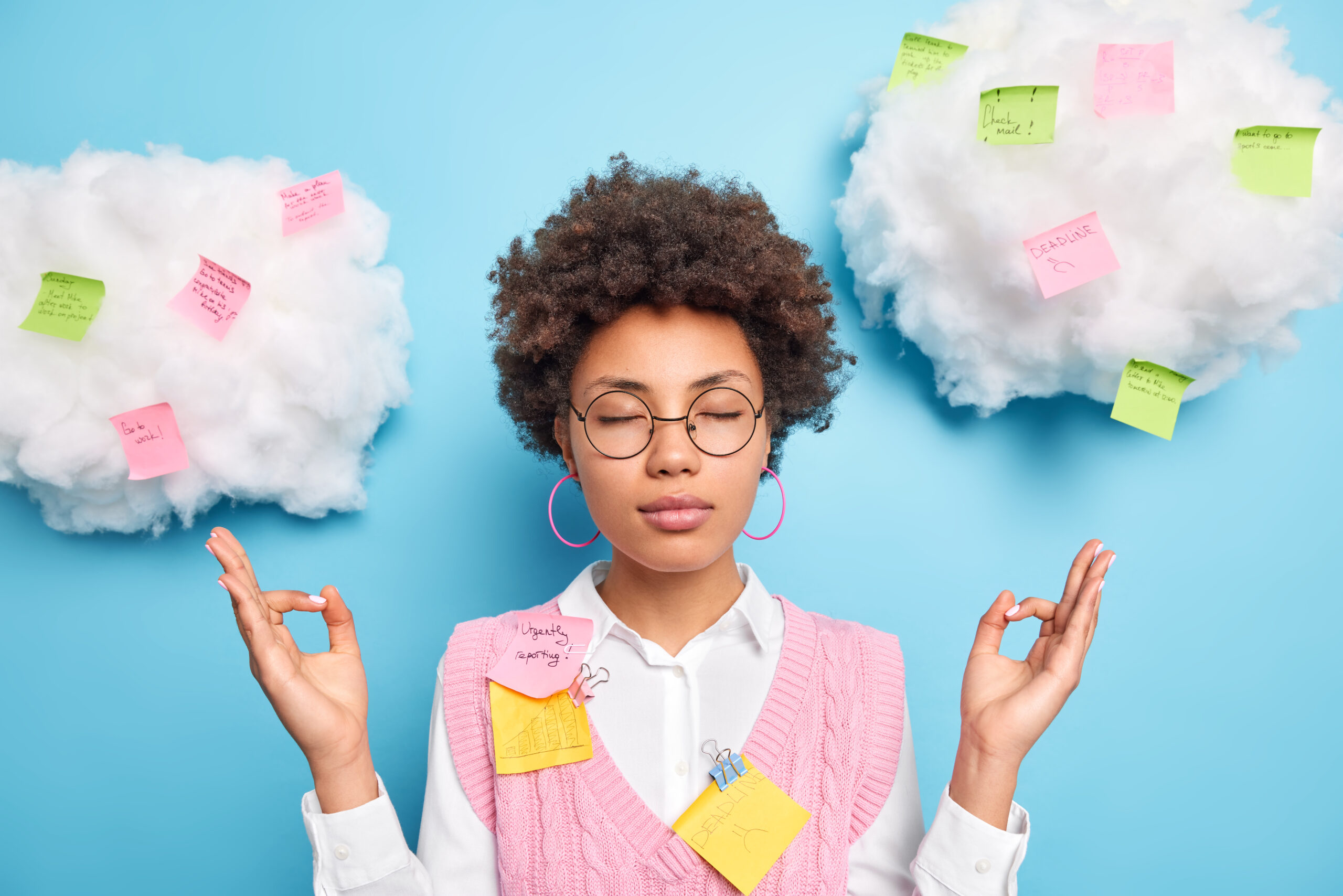Young woman meditating with sticky notes on clouds, symbolizing thoughts and tasks, against a blue background.