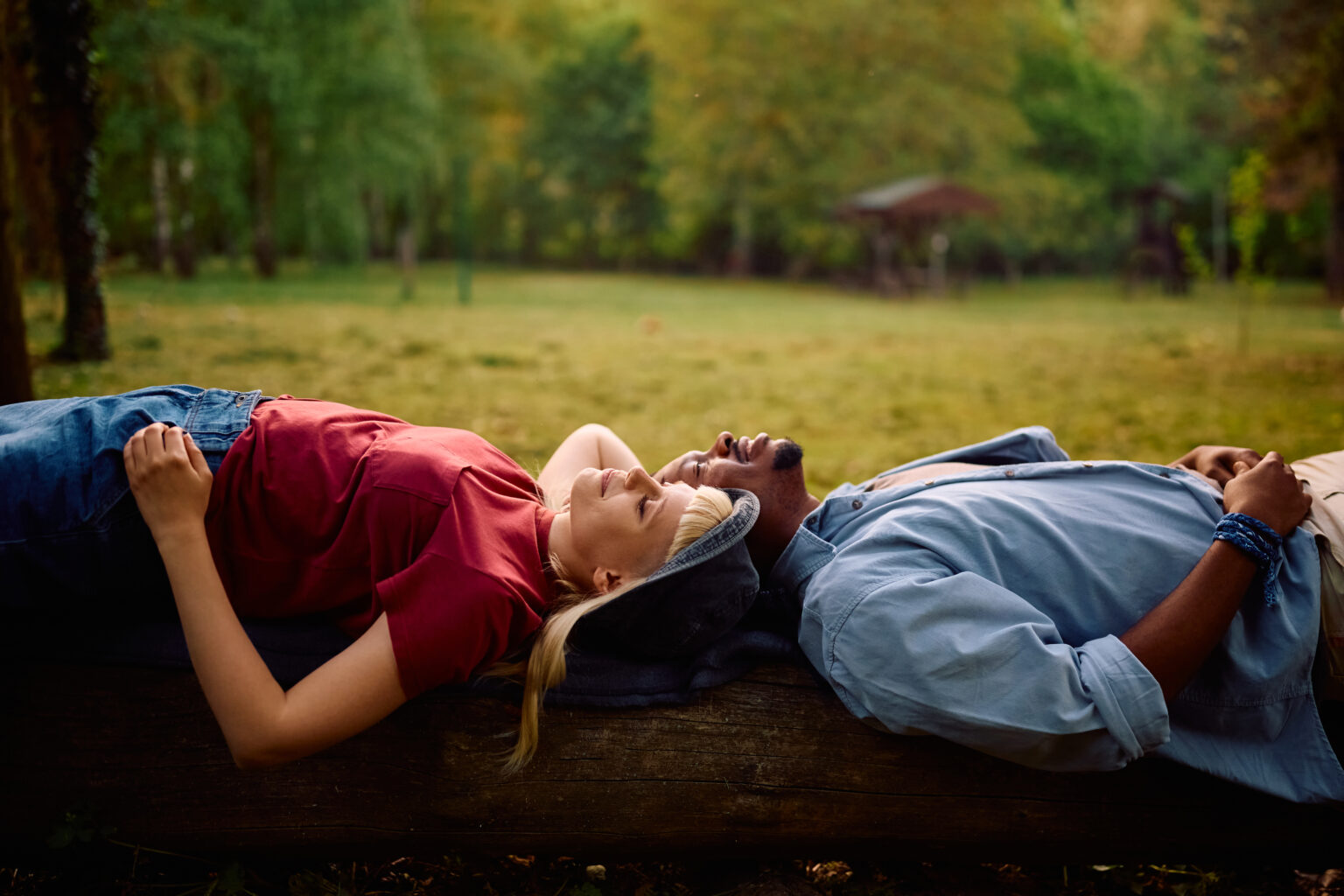 A woman and a man relax side by side on a log in a serene outdoor setting.