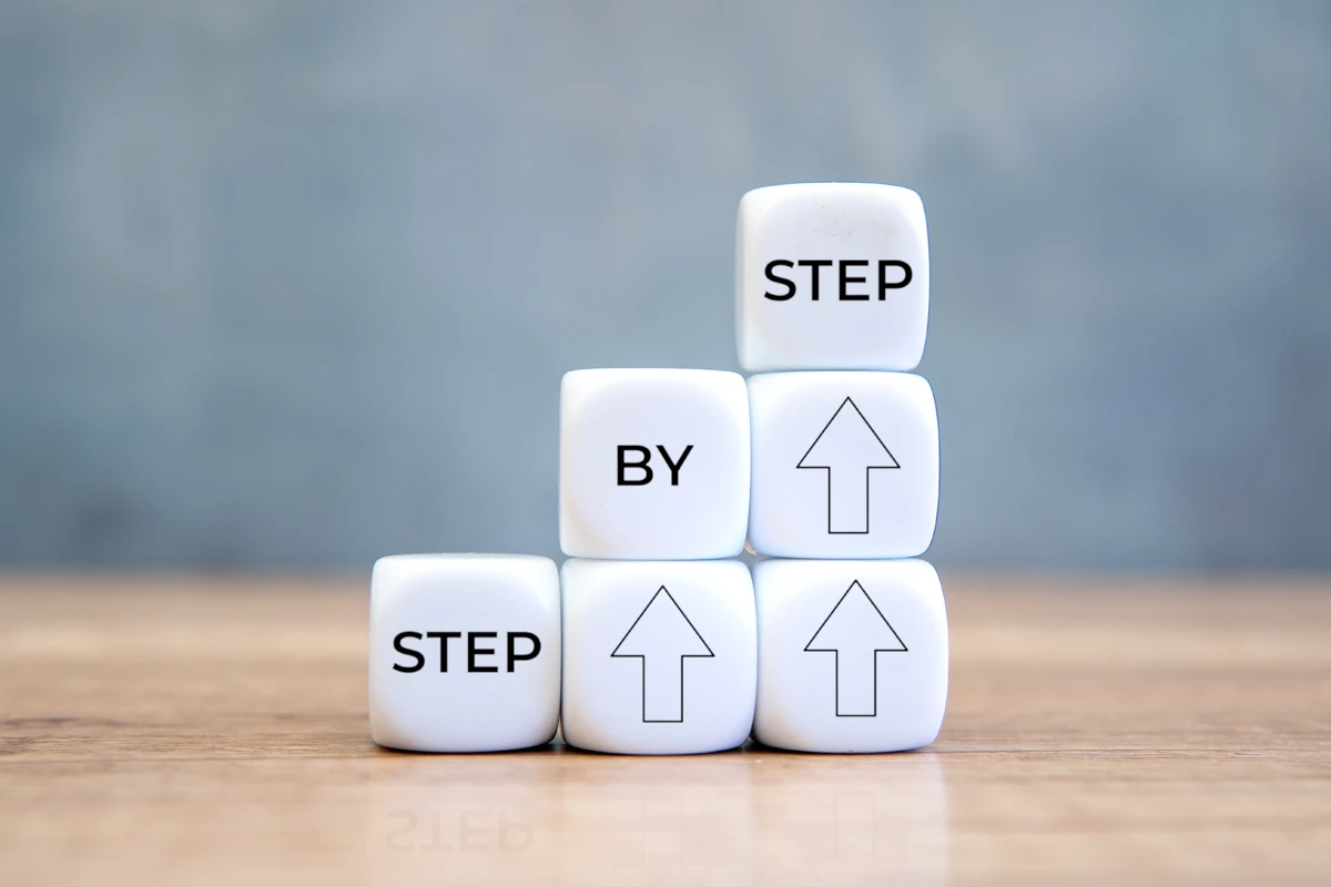 White dice stacked to spell "STEP BY STEP" with upward arrows, symbolizing progress and guidance.