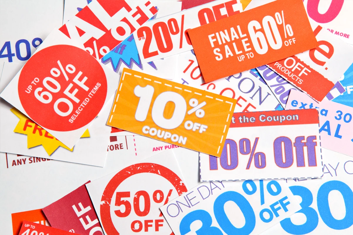 Colorful discount coupons and sale tags featuring various percentage off promotions scattered on a flat surface.