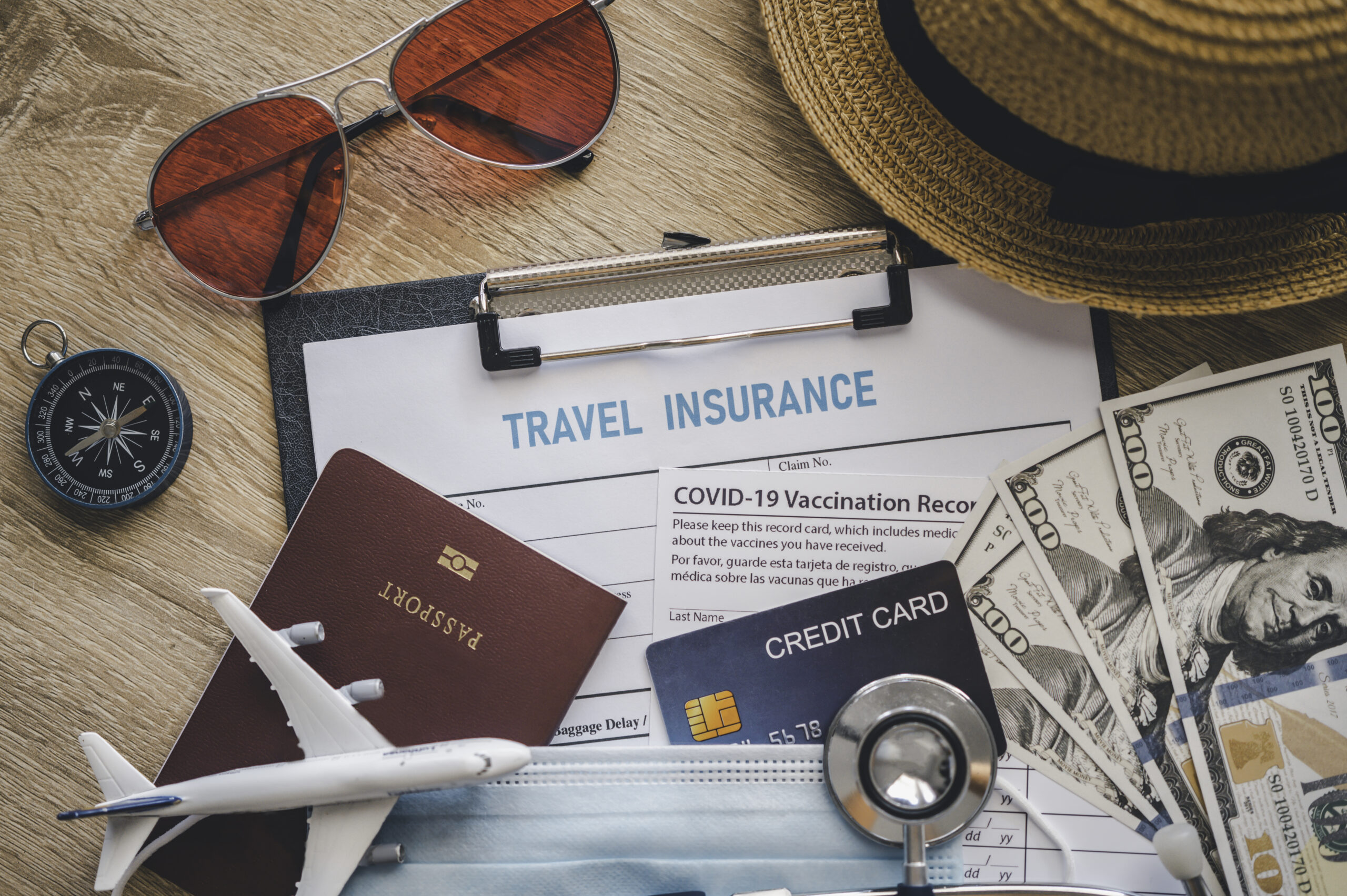 Travel essentials including a passport, travel insurance form, and cash on a wooden surface.
