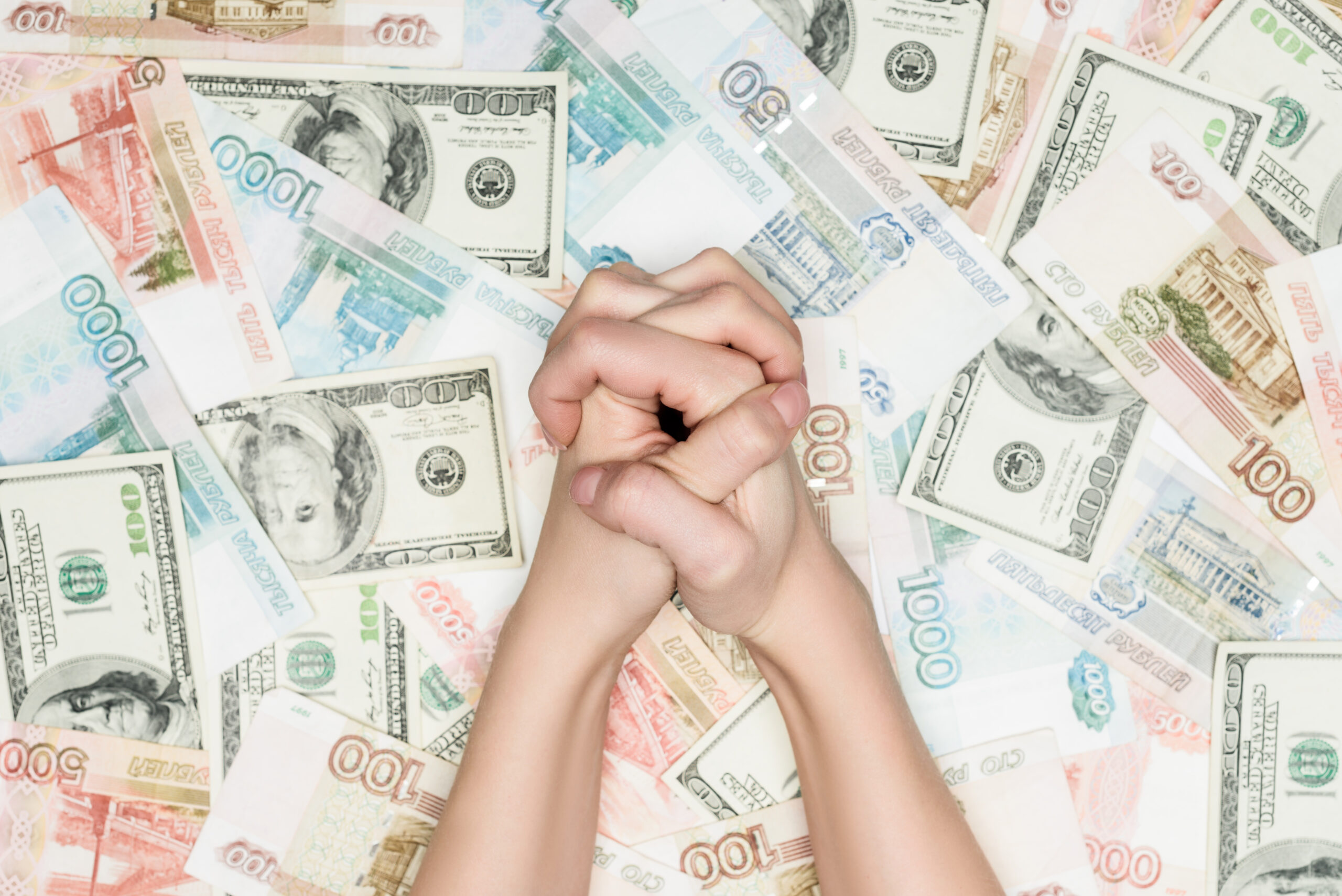 Hands clasped together over a spread of various banknotes from different currencies.