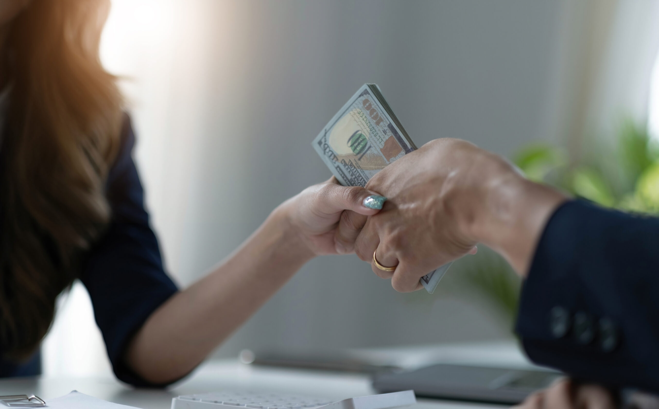Hands exchanging cash in a professional setting with a blurred background. best salary negotiations strategies