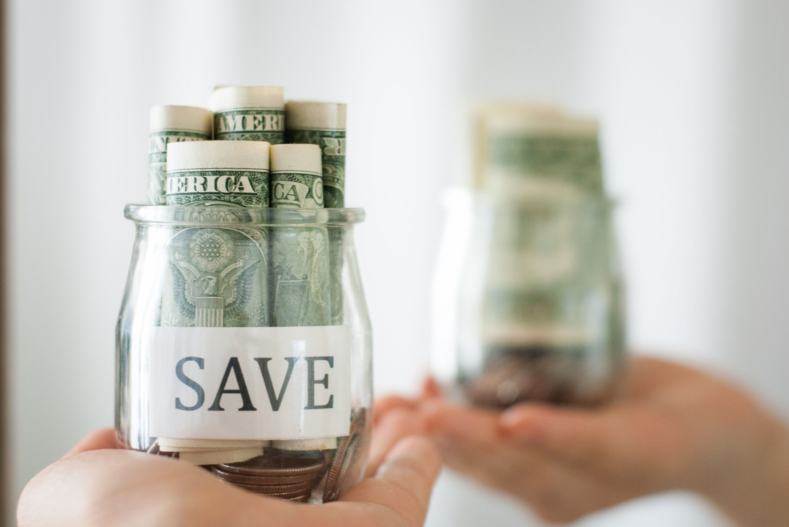 Glass jar labeled "SAVE" filled with rolled dollar bills and coins, held by a person.
