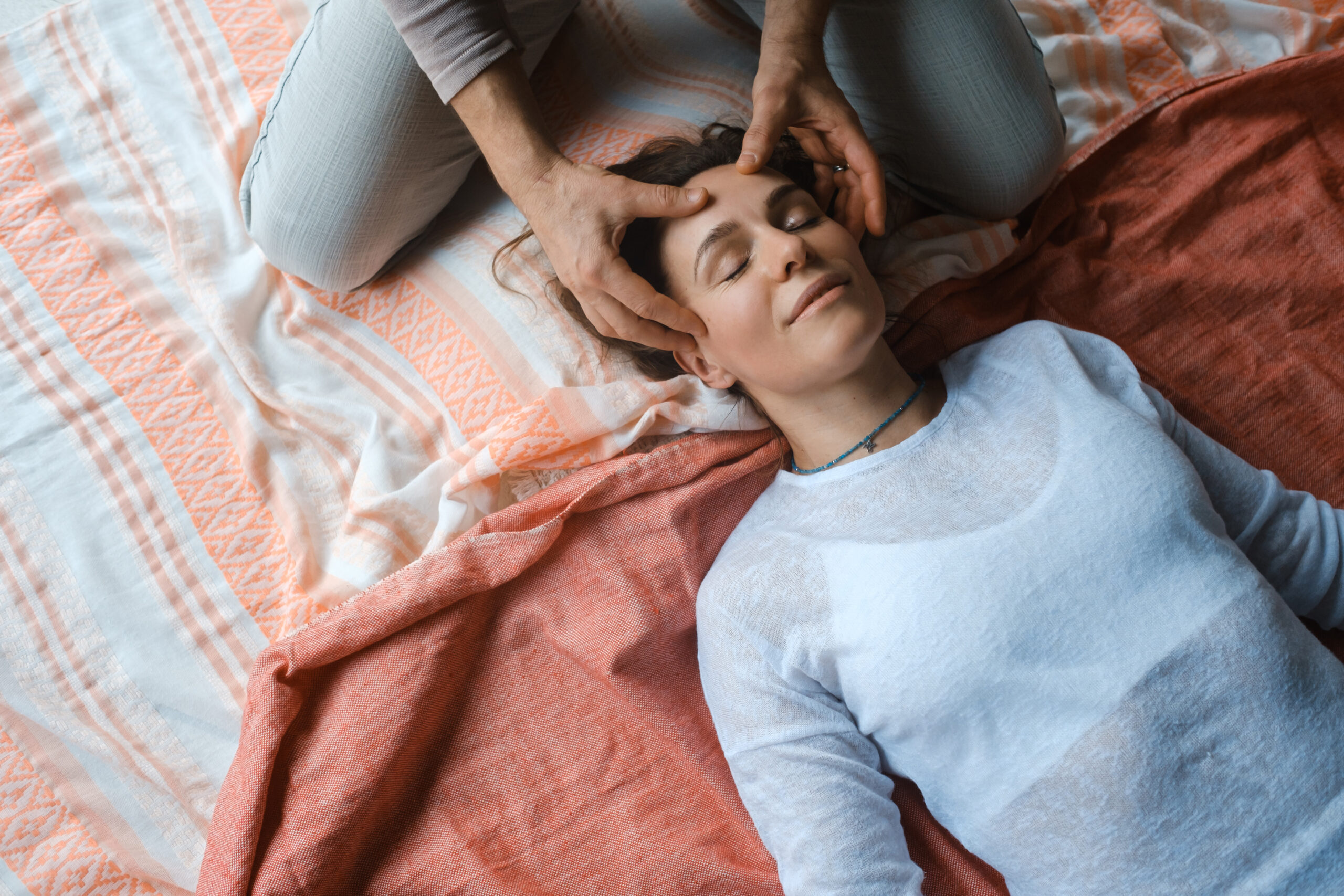 A person receives a relaxing head massage while lying on a patterned blanket.