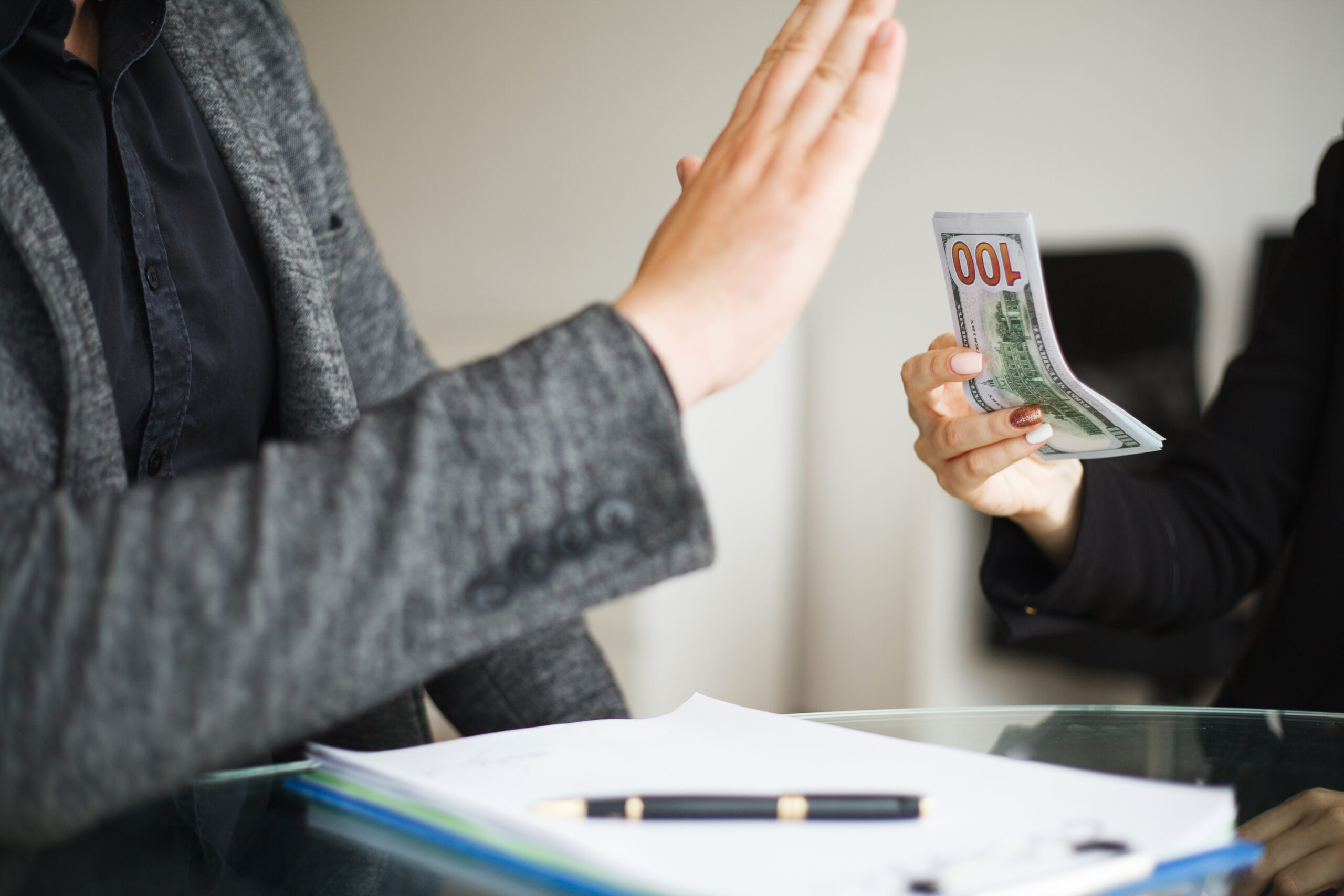 A person in a suit declines a cash offer while seated at a glass table with documents.