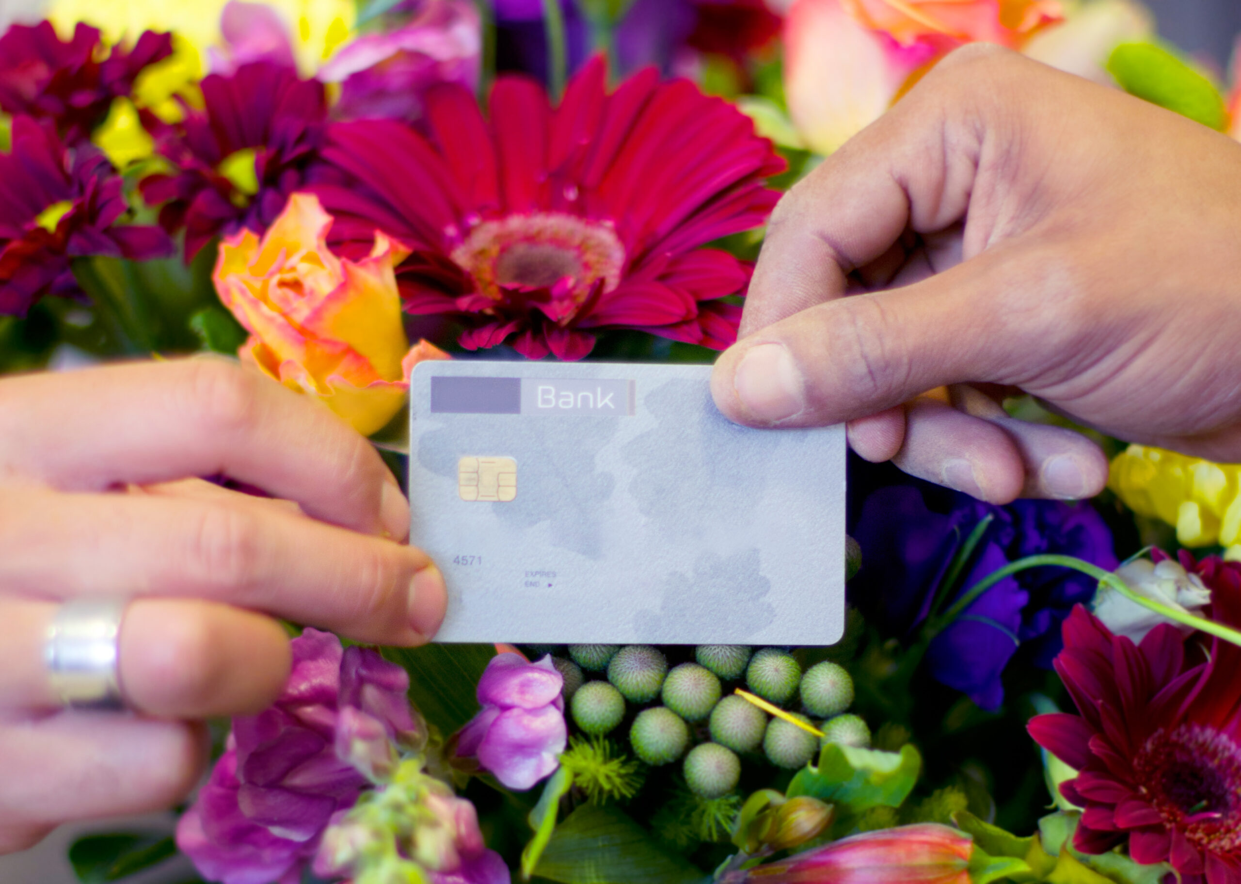 Hands exchanging a bank card amidst a vibrant bouquet of flowers.