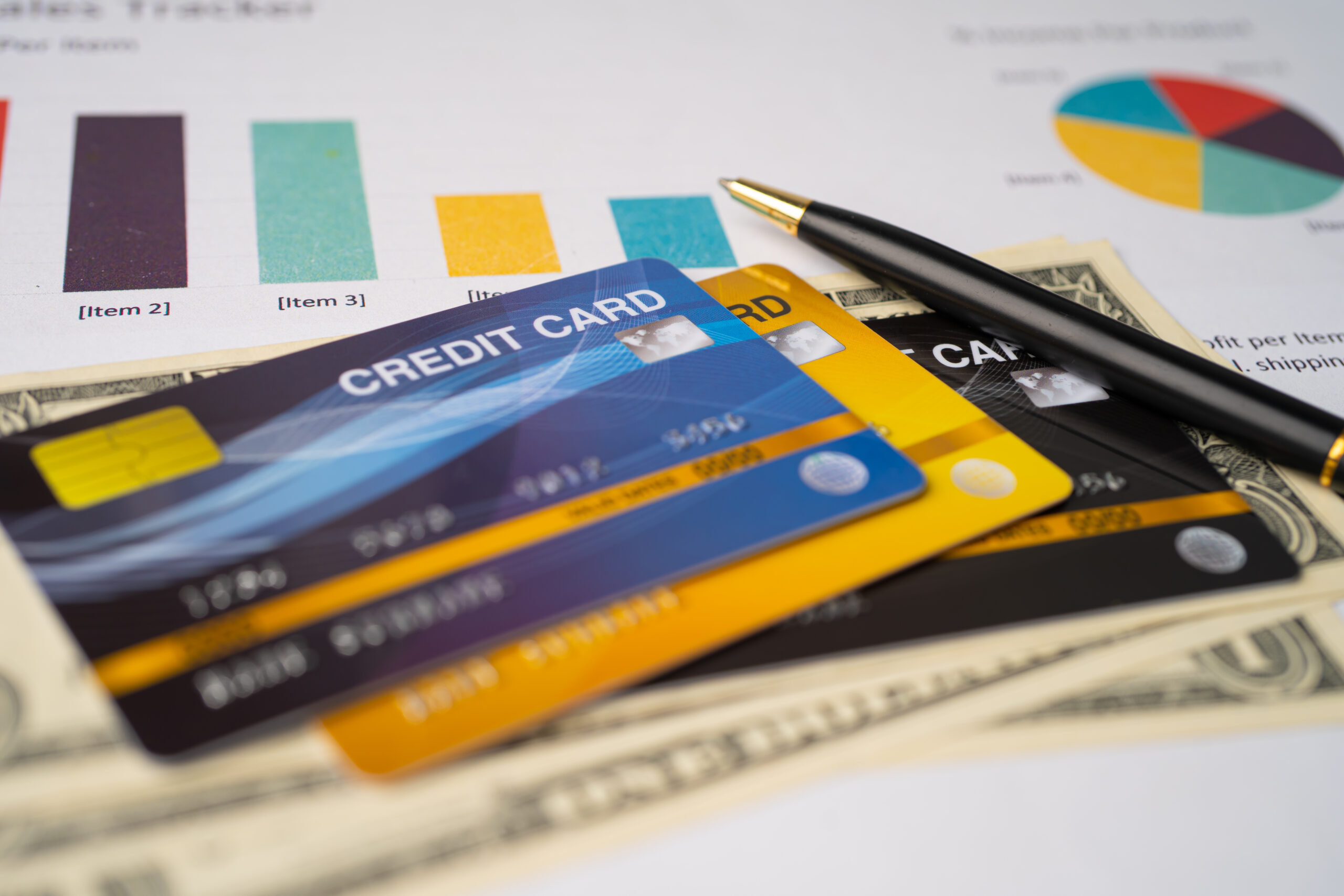 Credit cards and cash are arranged on a financial report with charts and graphs in the background. credit card myth