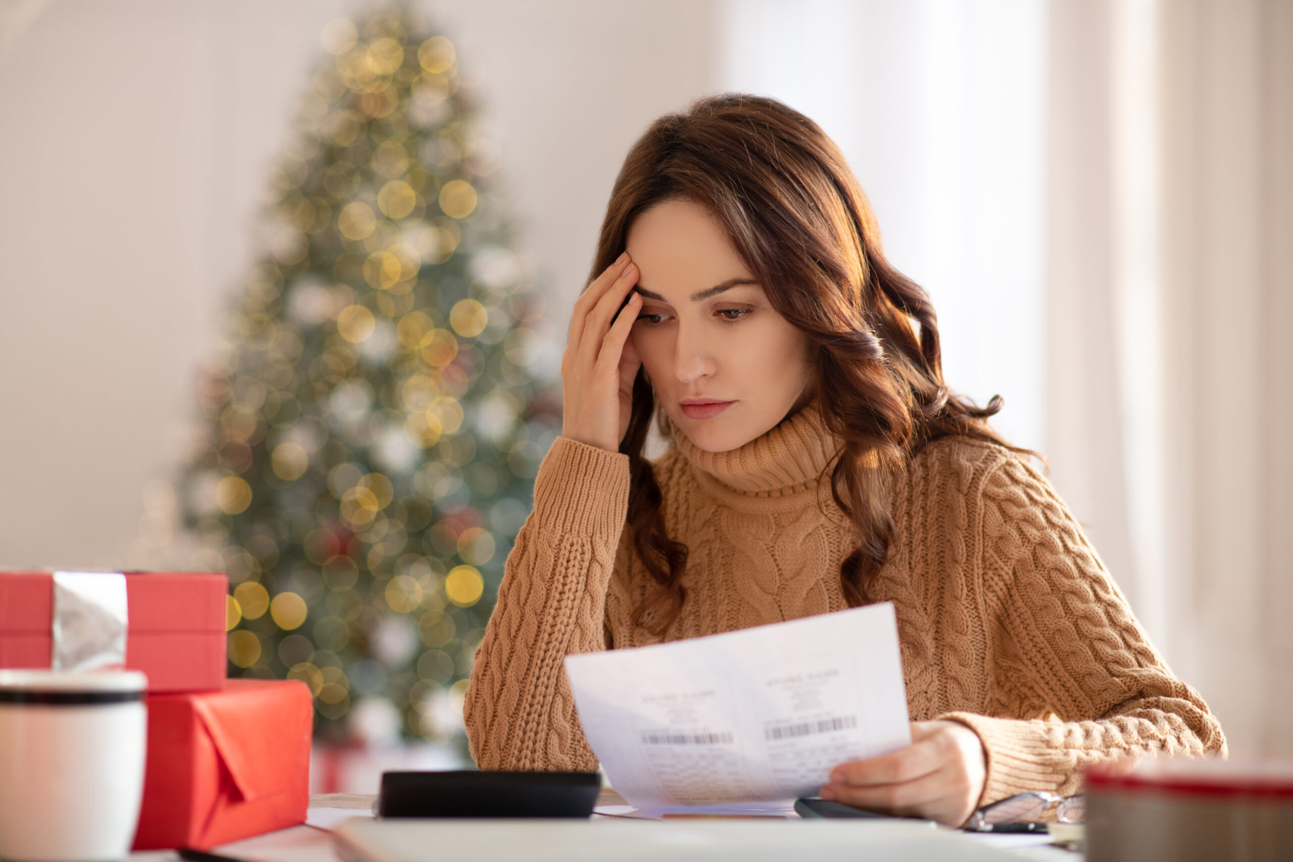 Woman in a cozy sweater looks stressed while reviewing documents at a table decorated for the holidays.