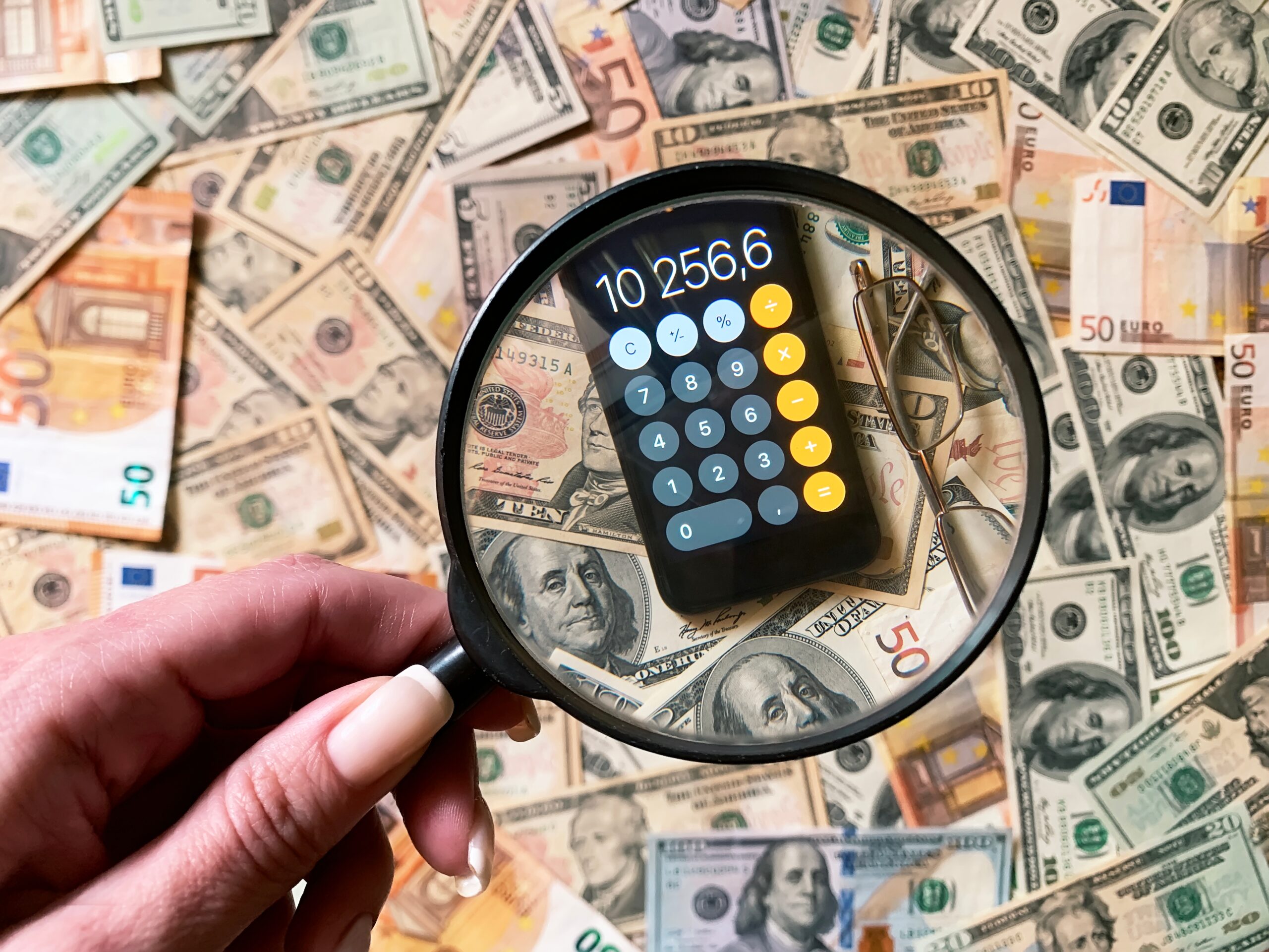A magnifying glass focuses on a calculator displaying a number, surrounded by various banknotes.