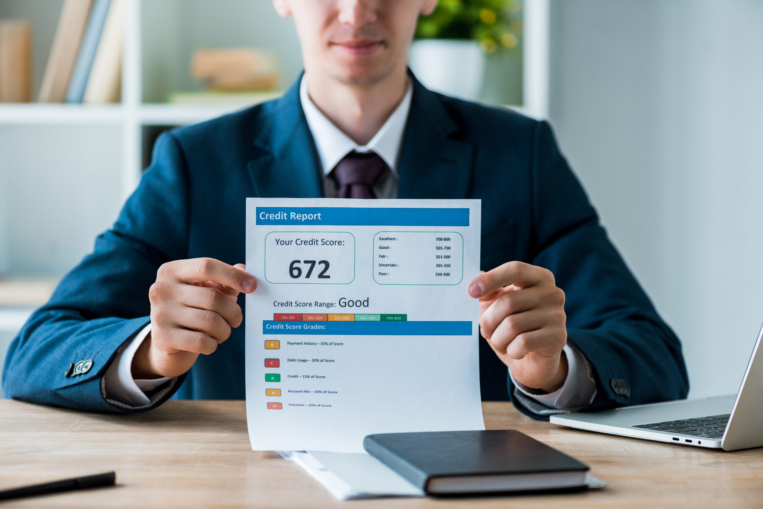 Man in a suit holds a credit report showing a score of 672, indicating a good credit range.