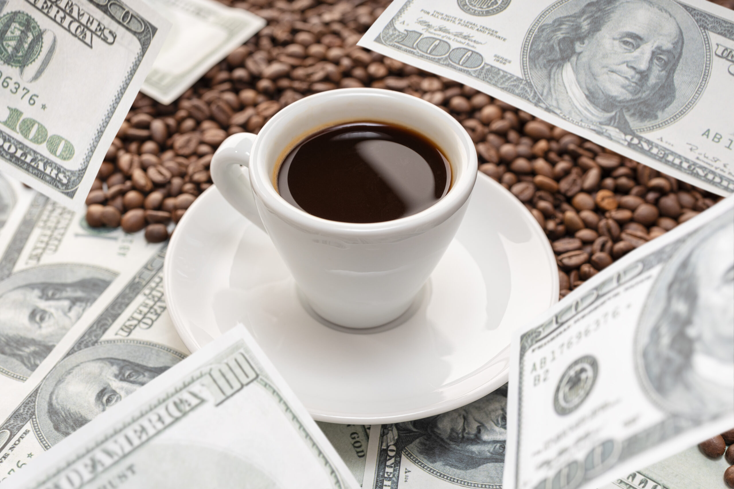 A cup of coffee surrounded by coffee beans and scattered hundred-dollar bills. cut out coffee and you can become a millionaire