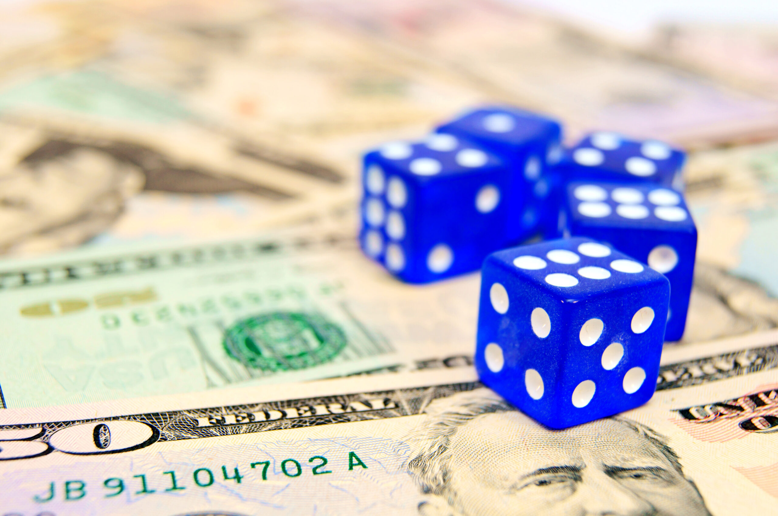 Blue dice scattered on a background of U.S. dollar bills. why investing is not gambling